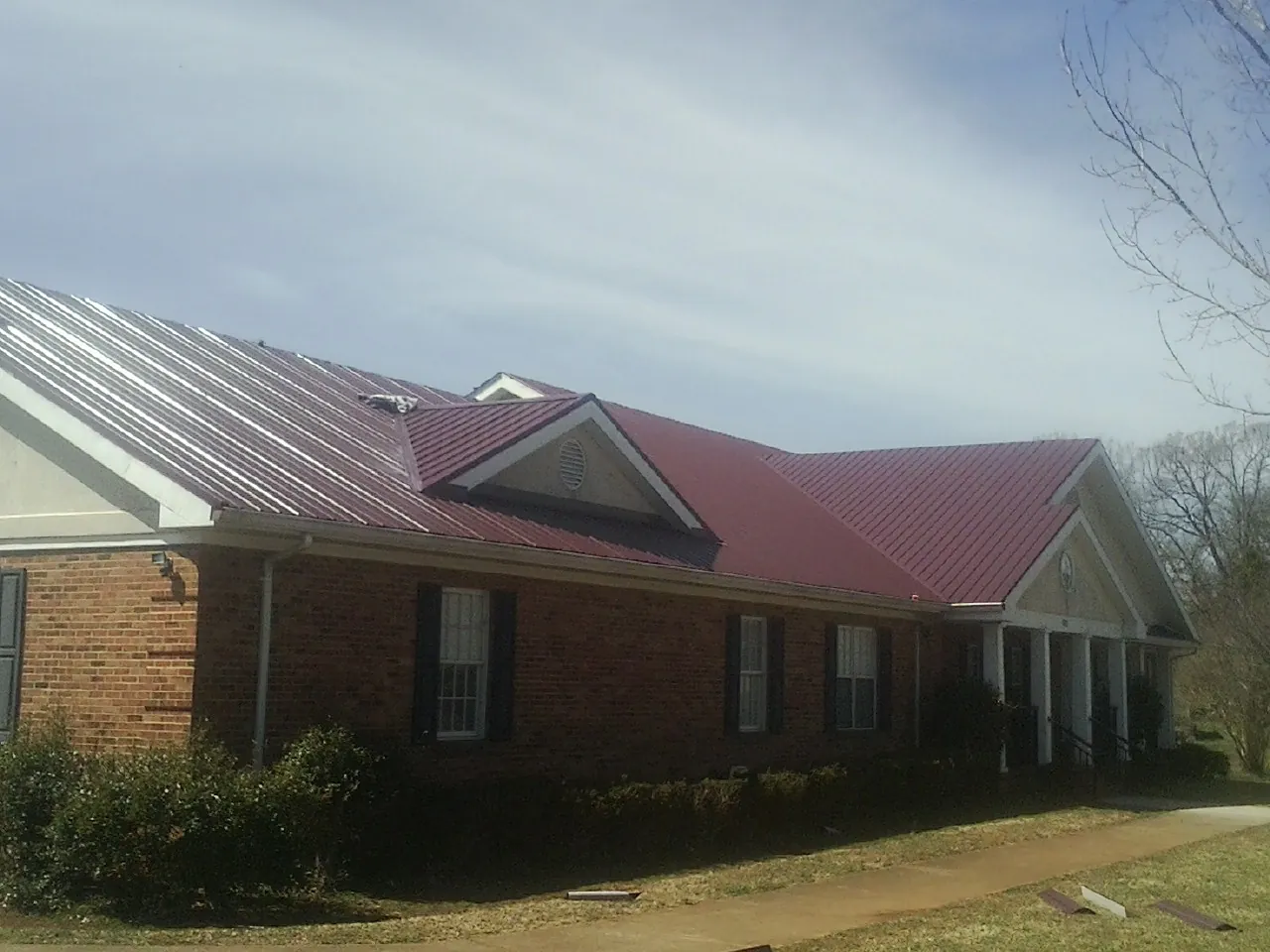 Red metal roof with gabled entries on a long brick building, from a Hail Damage Roof Repair job in Brookside