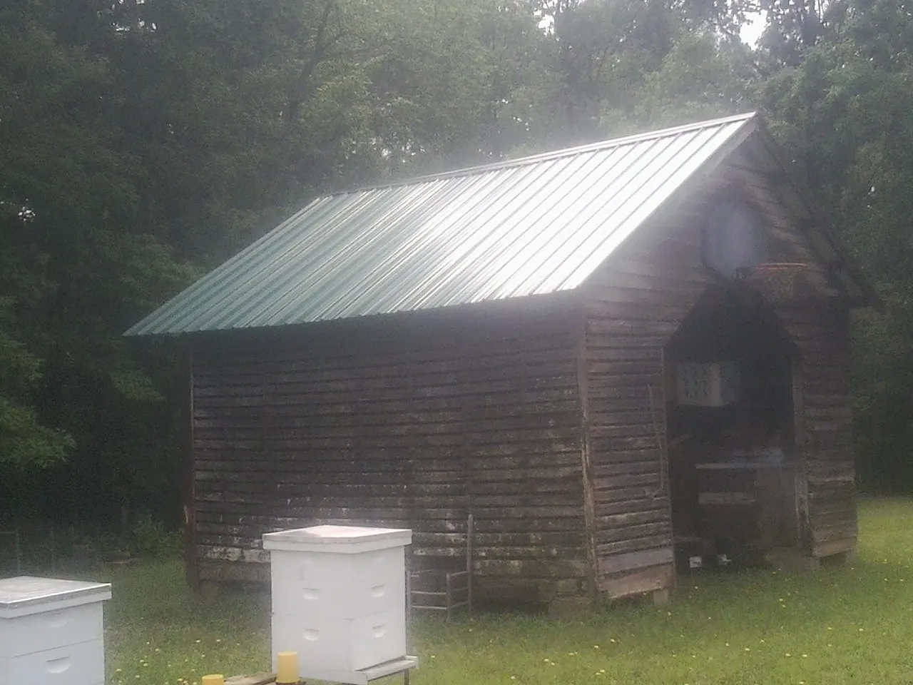 Green metal roof on a weathered barn beside stacked beehives in Brookside