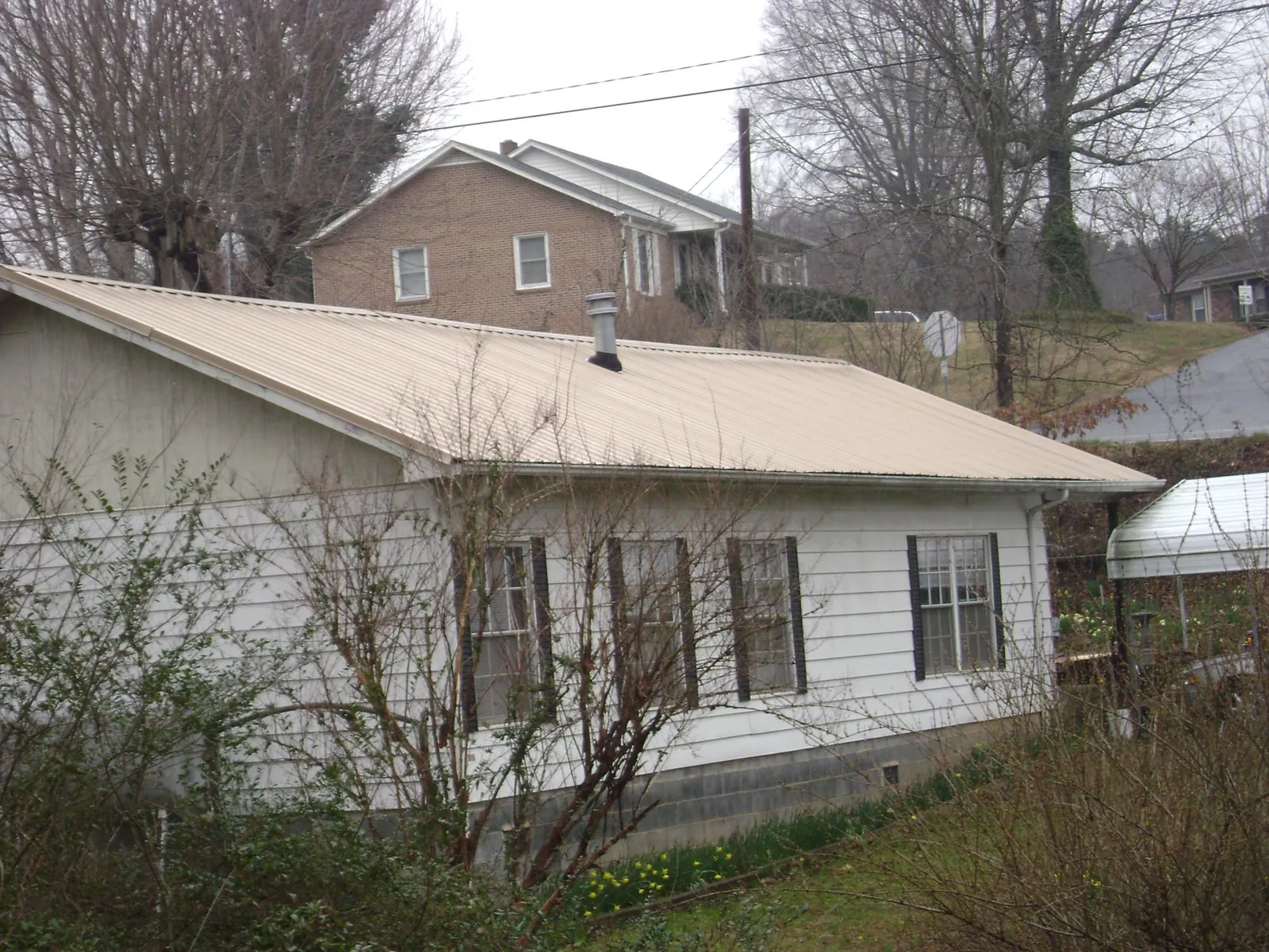 Tan metal roof on a white sided house set into a hillside — Commercial Roofing by Roofing Brothers in Brookside